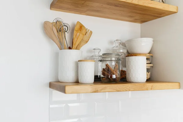 Kitchen shelves with various white ceramic and glass jars. Open shelves in the kitchen. Kitchen interior ideas. Eco friendly kitchen, zero waste home concept