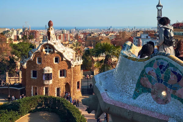 View from the mosaic Serpentine bench of the Park Guell to the Casa del Guarda gatehouse and panorama of the Barcelona city. — Stock Photo, Image