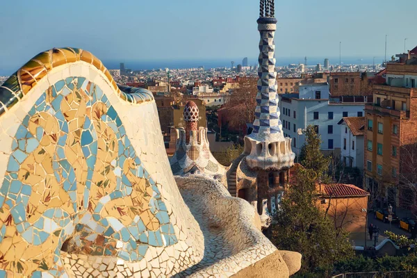 View from the mosaic Serpentine bench wall of the Park Guell to the pinnacle of administration office and panorama of the Barcelona city. — Stock Photo, Image