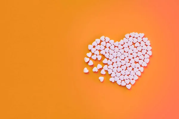 Beyaz kalp şekerler bir turuncu kağıt arka plan üzerinde şeklinde. Kırık kalp ya da pearts gethering aşk kavramı. Kopya alanı dahil. — Stok fotoğraf