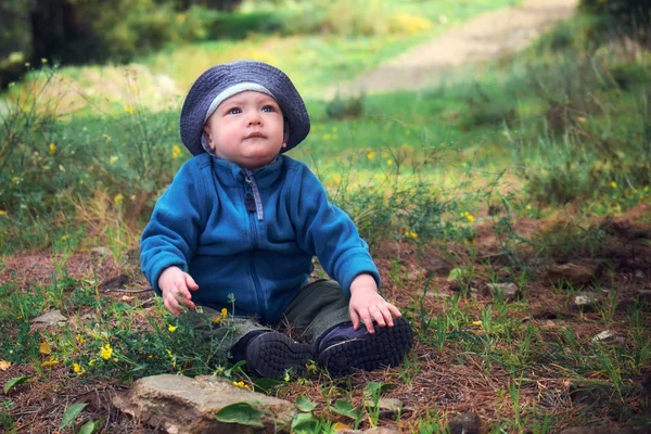 Ένα πορτρέτο από ένα χαριτωμένο μικρό αγοράκι τουρίστρια Εξερευνώντας τον κόσμο της φύσης κάθεται σε γρασίδι σε ένα δάσος σε ζεστό καιρό — Φωτογραφία Αρχείου