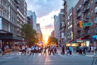 Manhattan 'da 23. Cadde ve 6. Cadde' nin kesiştiği yerde gün batımının renkli ışıklarıyla yürüyen bir grup insan.