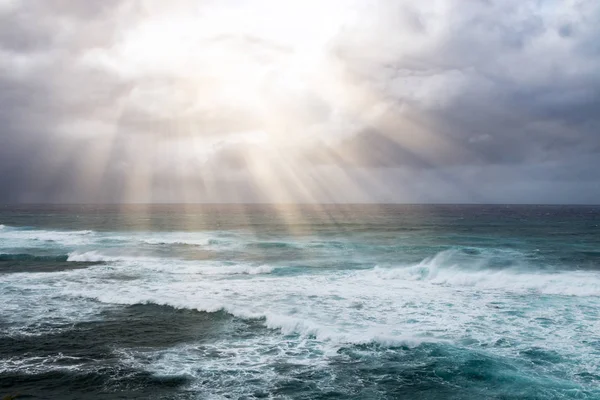 Rays of sunlight break through storm clouds above the open ocean waves in a heavenly seascape