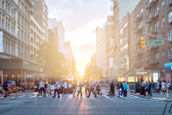 Diverse crowd of people walking across the busy intersection of 23rd Street and 6th Avenue in Manhattan New York City with the colorful light of sunset in the background