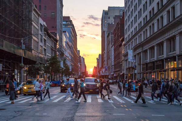 NEW YORK CITY - JUNE 7, 2018: The intersection of 23rd Street and Broadway is crowded with busy people and cars as the sun sets between the buildings of Manhattan in the background.