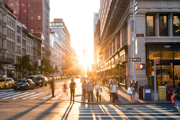 NEW YORK CITY, CIRCA 2018: Bright light of sunset shines on crowds of people crossing the intersection on 5th Avenue in Manhattan, New York City