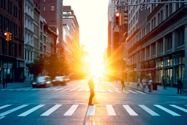 Blurred image of a man walking across the street in New York City with the bright light of sunset shining between the buildings