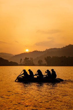 Grup hedef alacakaranlık, dağ ve güneş arka planda satır tekneye askerler yardım.