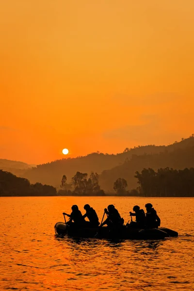 一群士兵帮助划艇瞄准在黄昏 山和太阳的背景下 — 图库照片