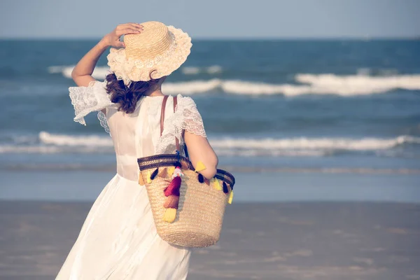 Woman wearing hat and holding bag on beach — Stock Photo, Image