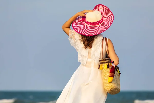 Woman wearing hat and holding bag on beach — Stock Photo, Image