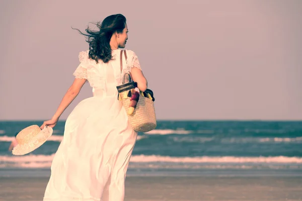 Nainen yllään hattu ja tilalla laukku rannalla — kuvapankkivalokuva