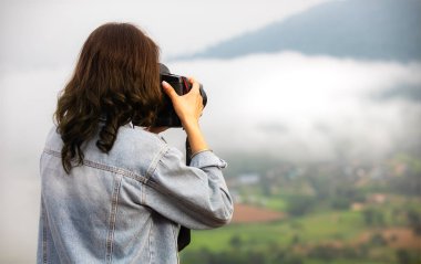 Doğa fotoğrafçısı kadın fotoğrafçı sabah yüksek yeşil bir dağın manzarasını çekerken arka planda beyaz, yumuşak bir sis bulutu vardı. Açık havada turistik yaşam tarzı için fikir