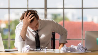 Masada tek başına oturan genç işadamı üzgün, ciddi ve iş sorunlarından dolayı stres hissederek ellerini tutuyor. Masanın üzerinde sarılı kağıtlar var..