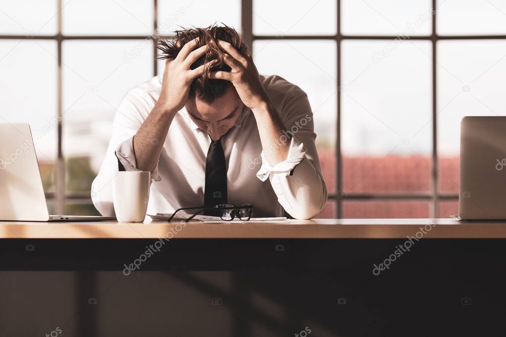 Young businessman sitting alone at desk and use hands holding his head feeling sad, serious and stress from work problems in office