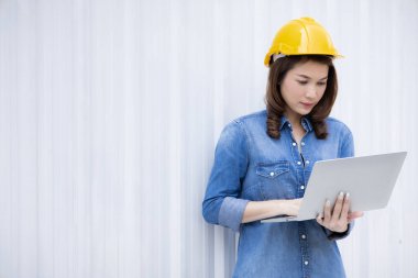 Kot pantolon giymiş güzel Asyalı kadın mühendis sarı güvenlik şapkası takıyor dizüstü bilgisayar kullanarak ofis dışında inşaat alanında iş yapıyor. Modern çalışan kadınlar için fikir.