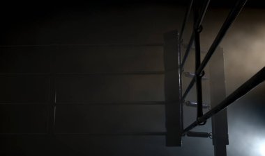 Bir boks ringinin loş bir köşesine dramatik bir şekilde yakın plan. Etrafı halatlarla çevrili, izole edilmiş karanlık bir zemin.