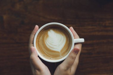 Bir beyaz kahve kupa tutan kadın el. Kahve kahvedir. Tablo üst görünümden alınan vintage tarzı ahşap tablo bkz: süt köpük köpük.
