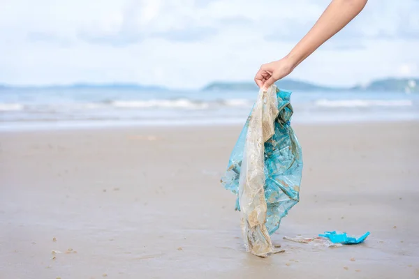 Woman���s hand picking up used plastic bag on sand beach, cleani — Stock Photo, Image