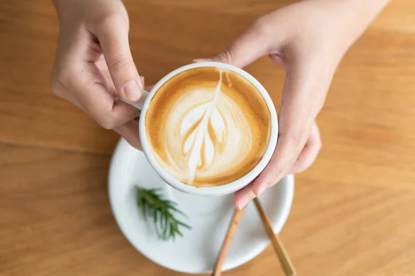 Woman hand holding a white coffee mug.  Coffee is a latte. table — Stock Photo, Image