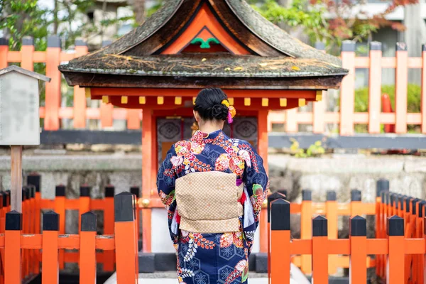 京都の伏見稲荷神社にある赤い木製の鳥居の中に日本の着物を着た芸者の女の子 着物は日本の伝統的な服です 着物という言葉は 実際には 着るもの を意味します — ストック写真