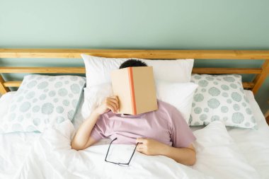 Asyalı yakışıklı adam uyurken kitap okur. Erkek kitap kapağı uykusuzluğa neden olur. Yeterli uyku kavramı. İyi uykular