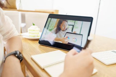 30-35 yaş arası Asyalı bir kadın tablet kullanıyor, evden gelen konferans videosu ve e-öğrenim konseptiyle iletişim kuran online dersler izliyor.