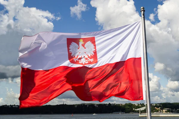 Polens flagga. Polens nationella flagga med emblem på molnigt blå — Stockfoto