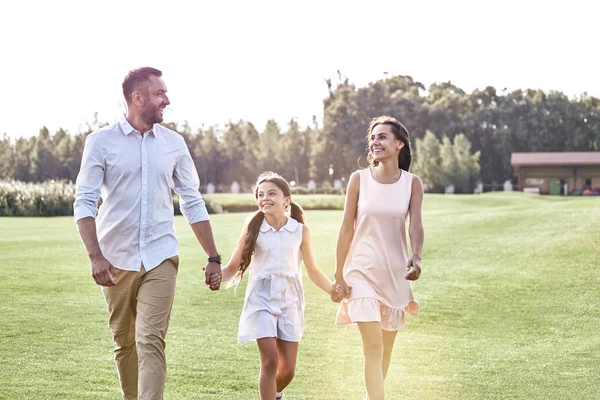 Family walk. Family of three walking on grassy field looking at