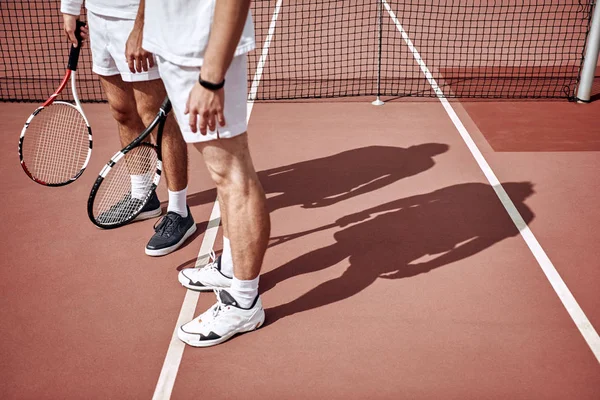Legs of tennis athletes on court. Cropped image