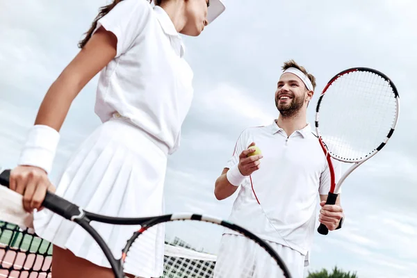 They play like a team. Beautiful young woman and man holding tennis racket and discussing set