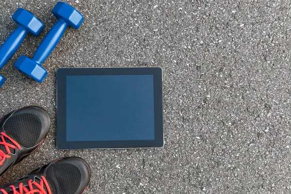 Smart sports gadgets. Cropped photo of dumbbells, water and black sneakers