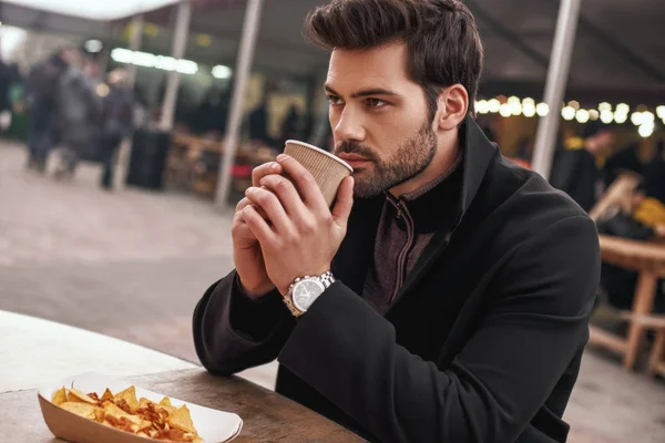 Side view of man drinking coffee near mexican food dish nachos con carne.