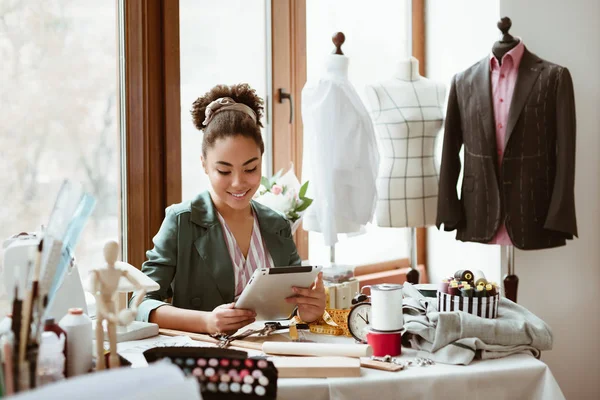 Design studio. Young woman tailor with digital tablet is modeling new clothes