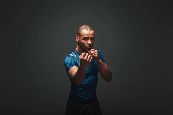 Come closer. Muscular boxer is ready to fight. Young sportsman standing over dark background