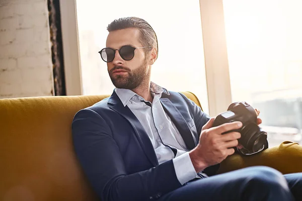 In search of inspiration. Successful young stylish businessman in sunglasses, is holding photo camera and thinking about something
