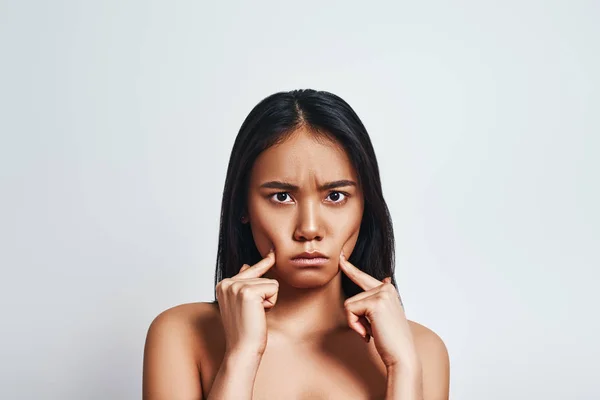 In a bad mood. Upset young asian woman making a face and feeling sad while standing against grey background. Negative emotions