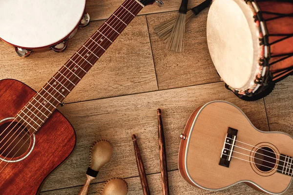 Ethnic musical instruments set: tambourine, wooden drum, brushes, wooden sticks, maracas and guitars laying on wooden floor. Top view