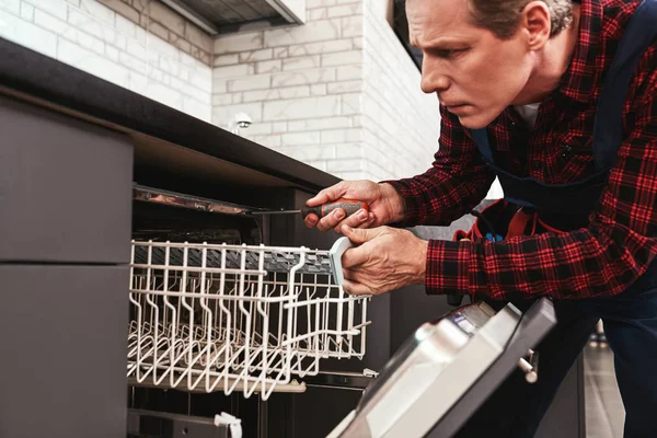 Repairing dishwasher. Male technician sitting near dishwasher