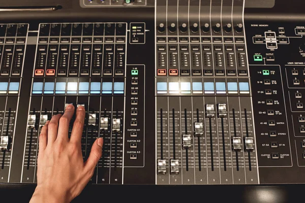 Professional sound control. Close-up view of male hand mixing sounds on digital audio mixing console with many buttons and shaders.