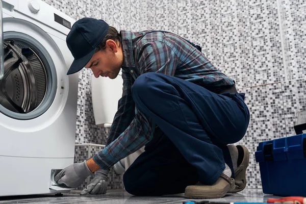 Attantive worker. Working man plumber in bathroom checking washing mashine