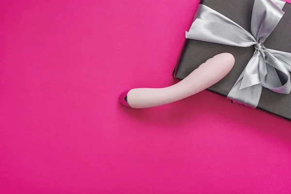 Intense orgasm. Pink g-spot vibrator and black gift box arranged on a pink background