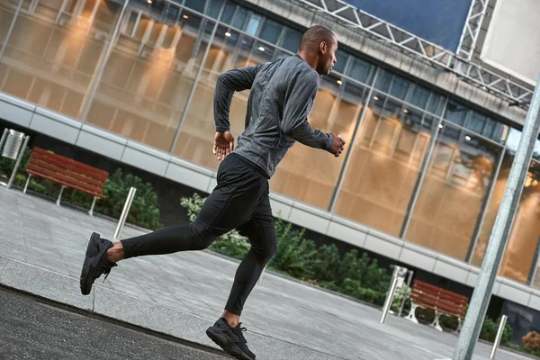 Healthy habits. Full length of young and athletic african man in stylish sportswear running in the city while his morning workout. Side view