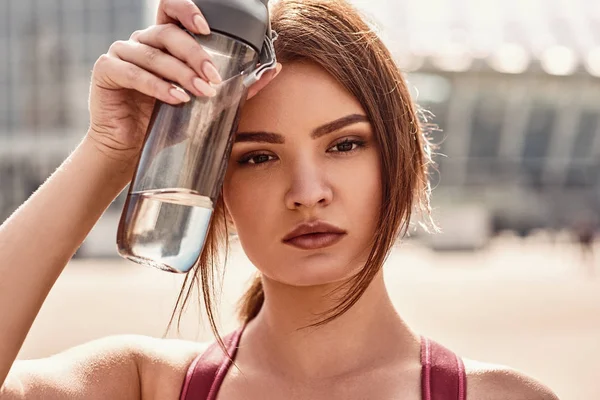 Water is energy. Close up portrait of beautiful woman holding bottle of fresh water and resting after active morning workout