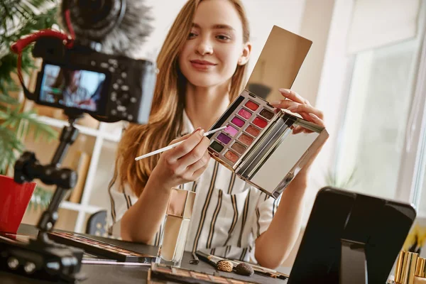 Choose it. Cute female blogger presenting a makeup palette and smiling while looking at camera