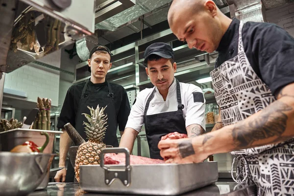 Right choice. Professional chef in apron holding a red meat and teaching his assistants how to choose it for cooking