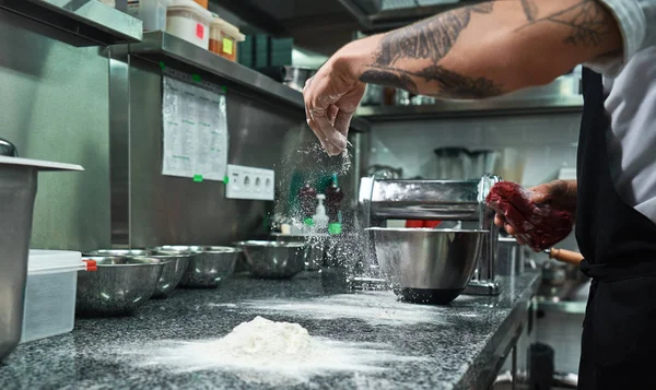 Cooking process. Male chef hands with black tattoos pouring flour on kitchen table