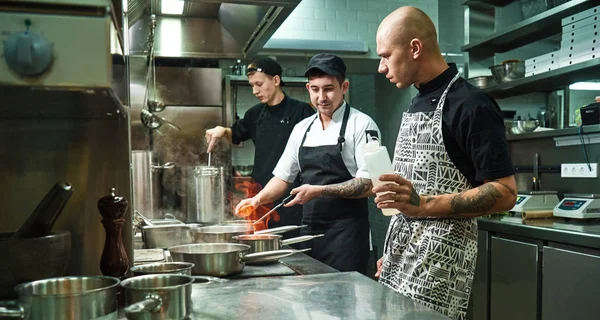 Dangerous work. Profesional chef teaching his two young trainees how how to flambe food safely. Cooking techniques