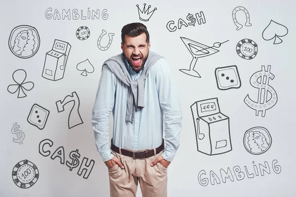 Bad luck. Angry young man keeping hands in his pockets and shouting while standing against grey background with different doodle illustrations on it. Gambling concept. Money