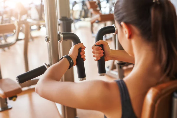 Sport everyday. Back view of young woman is working out at gym. Doing exercises on the simulator